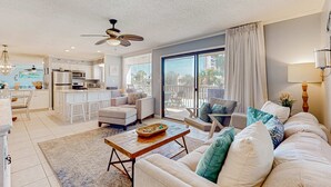 A spacious living room with a large sofa, a coffee table, and a dining area with a kitchen in the background. - 2nd-floor condo with beach access, pool, tennis courts, & on-site laundry (Destin)