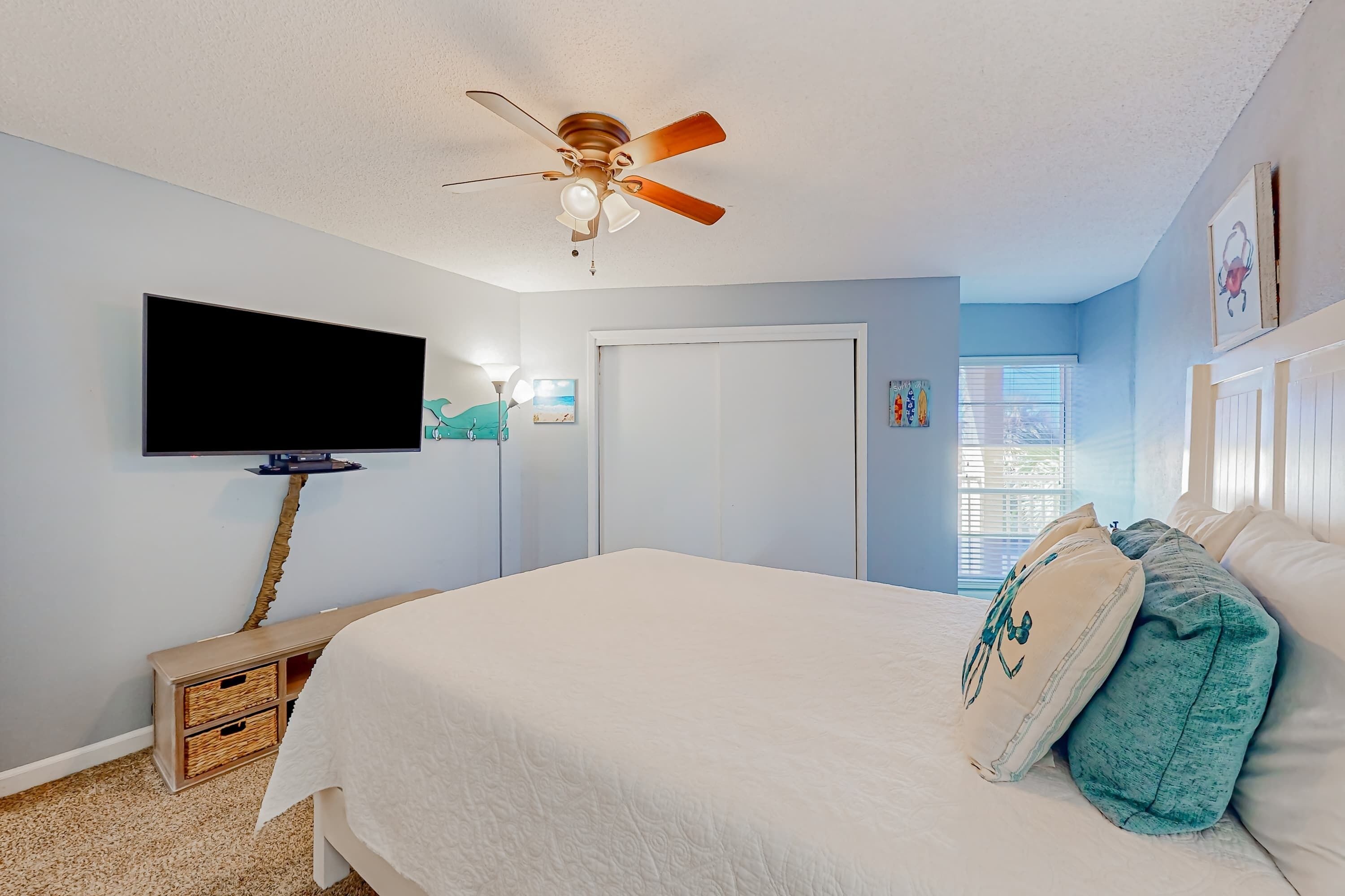A bedroom with a bed, a ceiling fan, a television, and a door.