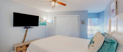 A bedroom with a bed, a ceiling fan, a television, and a door.