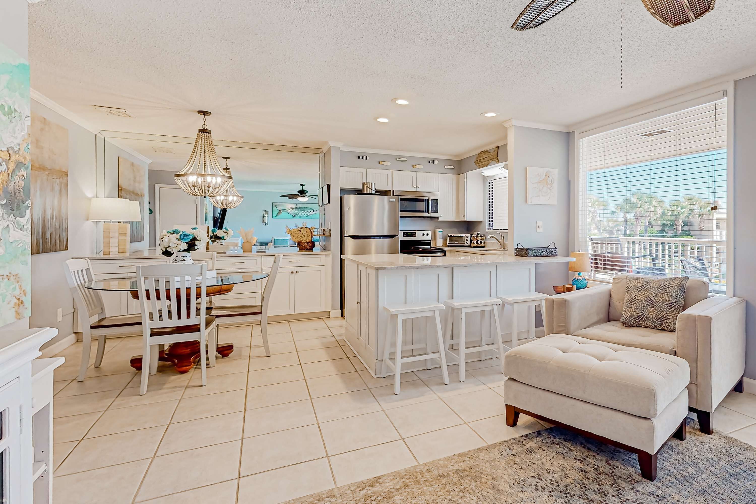 A modern kitchen with white cabinetry, a central island, and a dining area with a glass table and white chairs.