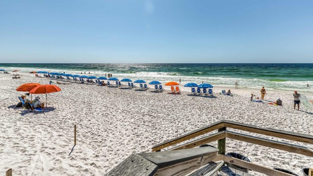 A beach with rows of blue and orange umbrellas, a wooden walkway, and people relaxing on the sand. - Ocean-view condo with pool, sauna, tennis courts & private beach access (Destin)