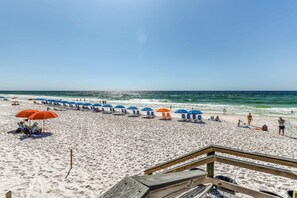 A beach with rows of blue and orange umbrellas, a wooden walkway, and people relaxing on the sand. - Ocean-view condo with pool, sauna, tennis courts & private beach access (Destin)