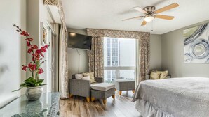 A bedroom with a bed, a sofa, a TV, and a window with curtains. - Ocean-view condo with pool, sauna, tennis courts & private beach access (Destin)