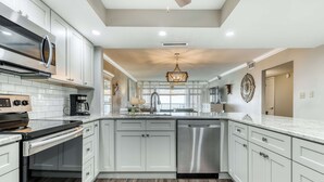 A modern kitchen with white cabinetry, stainless steel appliances, and a marble countertop. - Ocean-view condo with pool, sauna, tennis courts & private beach access (Destin)