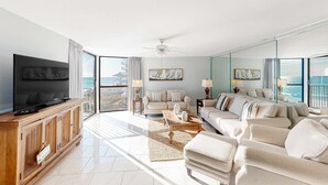 Amplia sala de estar con una gran televisión de pantalla plana, un conjunto de sofá, una mesa de centro y vista al océano a través de amplias ventanas.