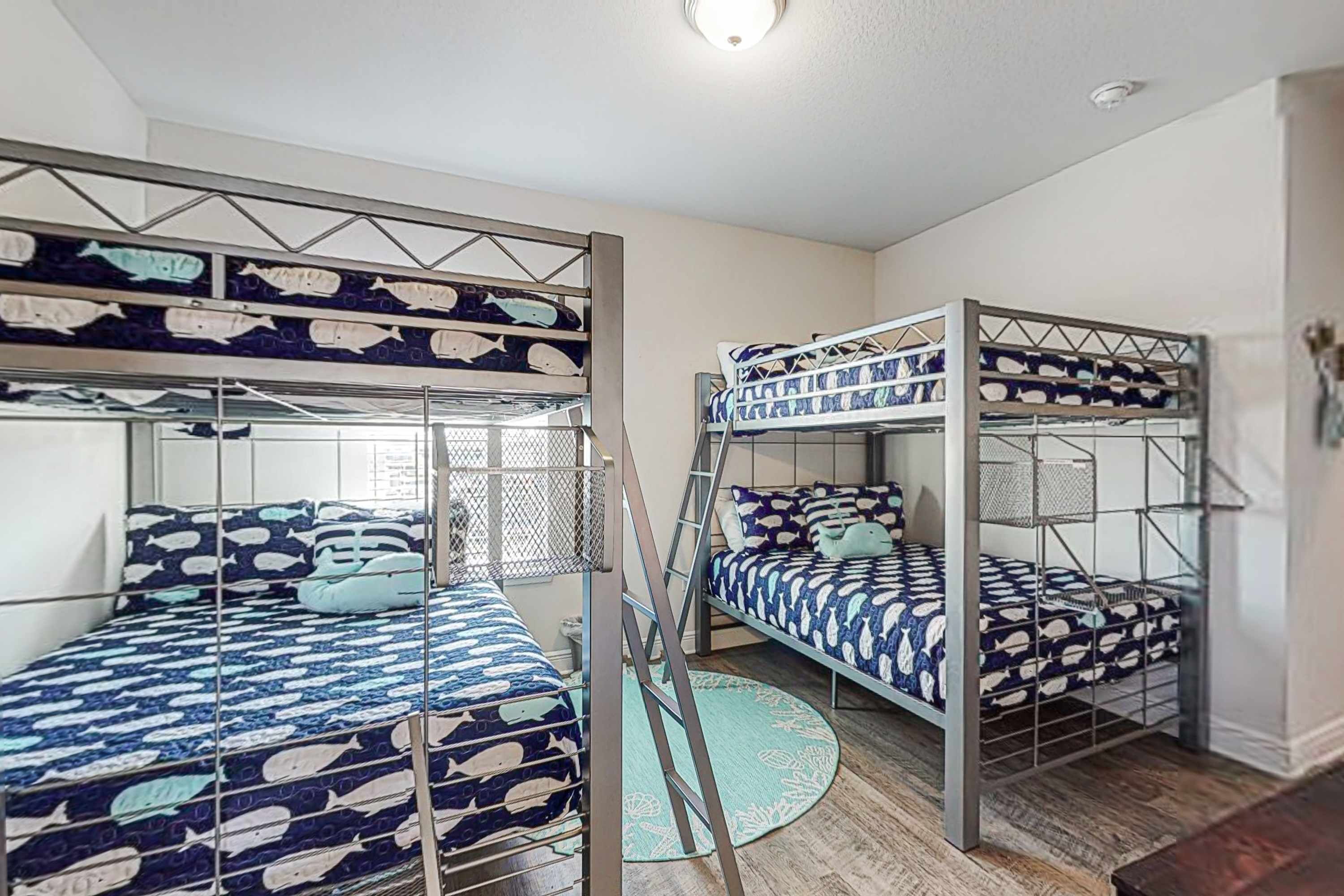 A dormitory room with bunk beds, a round rug, and a window with blinds.