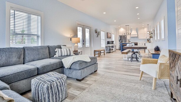 Ein geräumiges Wohnzimmer mit grauem Sofa, Hocker und einem Essbereich mit Tisch und Stühlen.