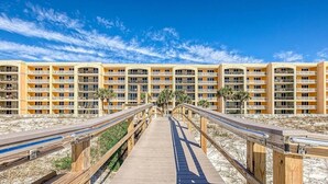 A wooden boardwalk leading to a multi-story hotel with balconies and palm trees. - Azure 202-Newly Refreshed 2026 (Fort Walton Beach)