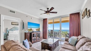 A spacious living room with a large sofa, a coffee table, and a television. There is a balcony with a view of the ocean. - Azure 202-Newly Refreshed 2026 (Fort Walton Beach)