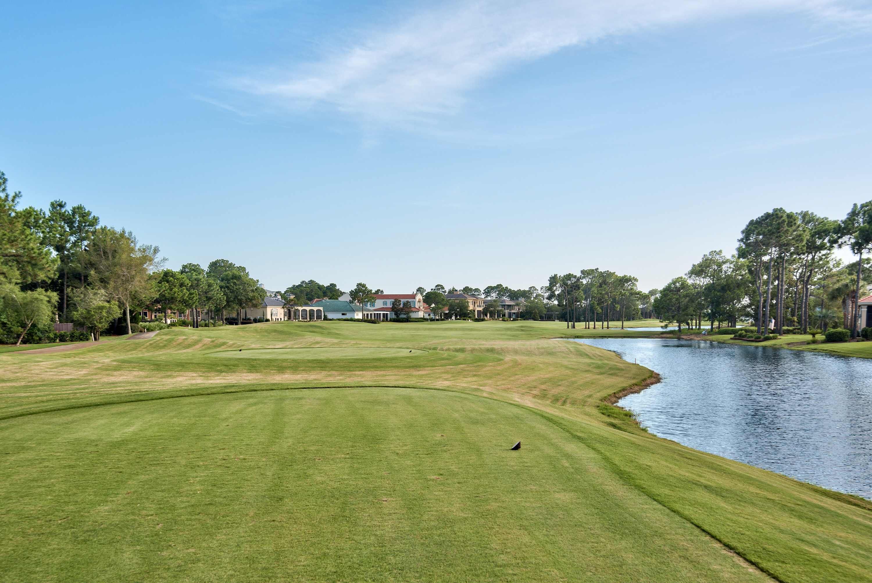Un terrain de golf avec un étang, des maisons en arrière-plan et des arbres.