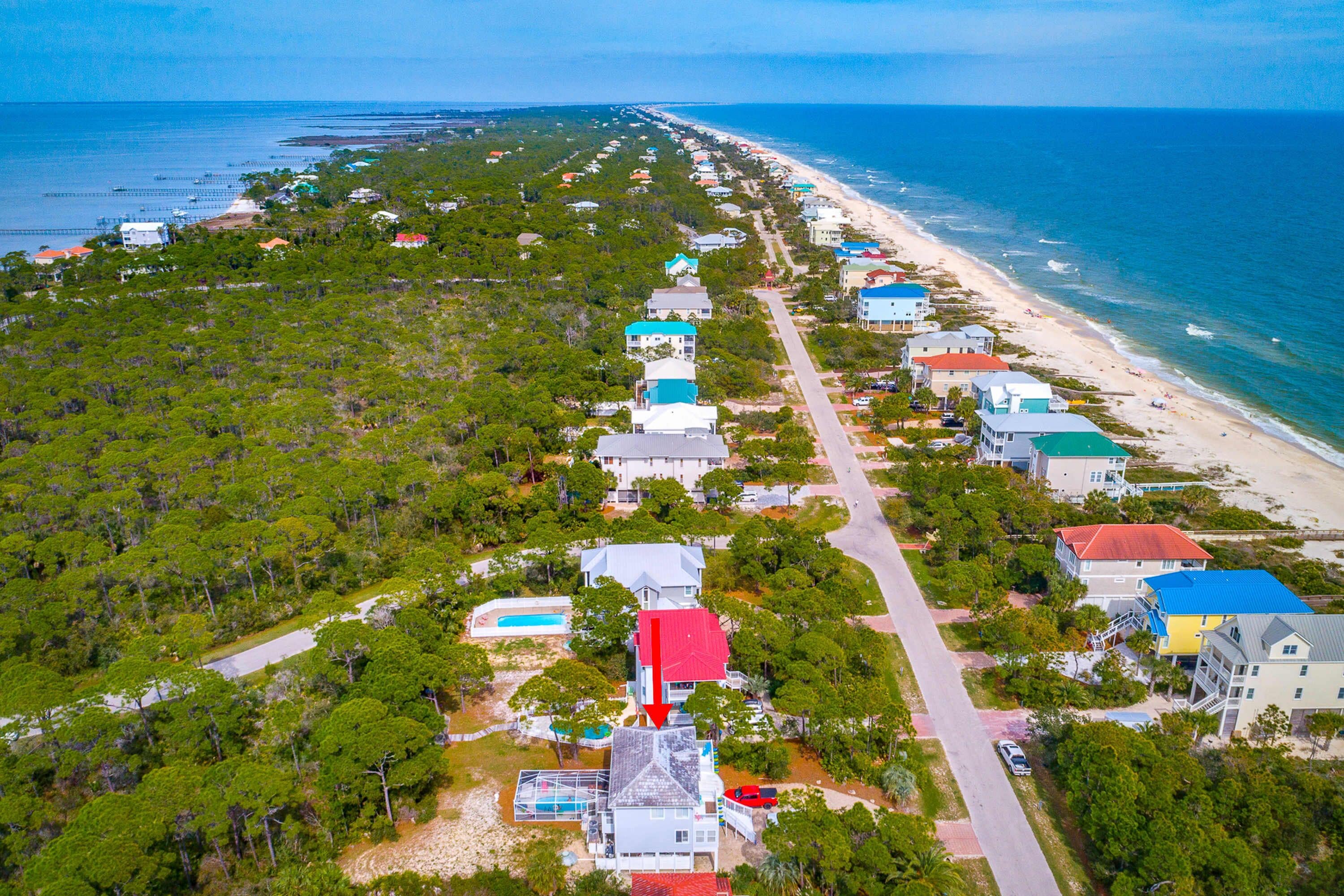 An aerial view of a coastal residential area with houses along the beach, surrounded by dense greenery.