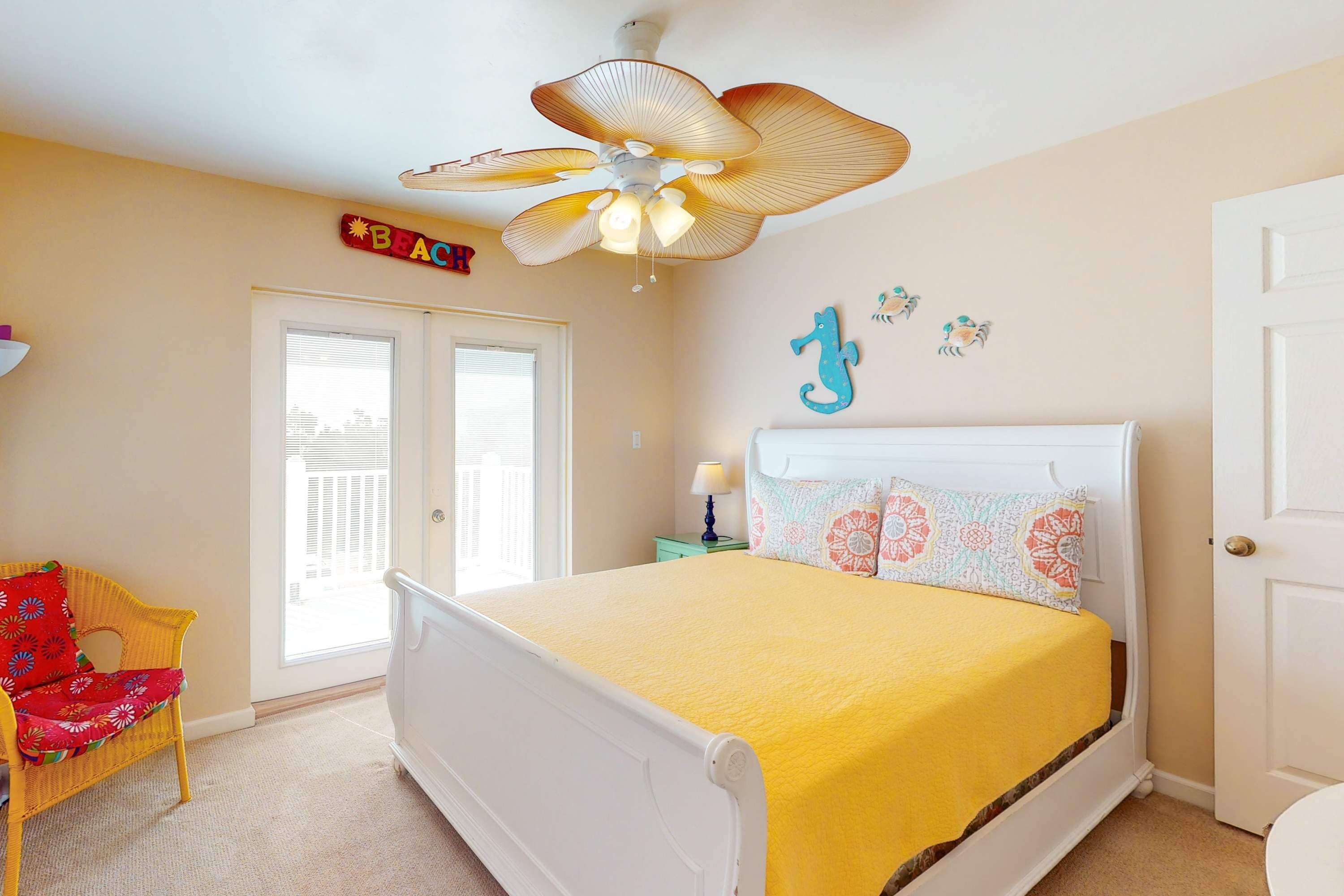 A bedroom with a bed, a chair, a ceiling fan, a door, and a wall decoration.