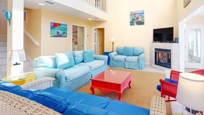 A spacious living room with light blue sofas, a red coffee table, and a fireplace. - Beach Across the Street! Dog-Friendly Home with Private Pool, AC, WiFi & Games! (St. George Island)
