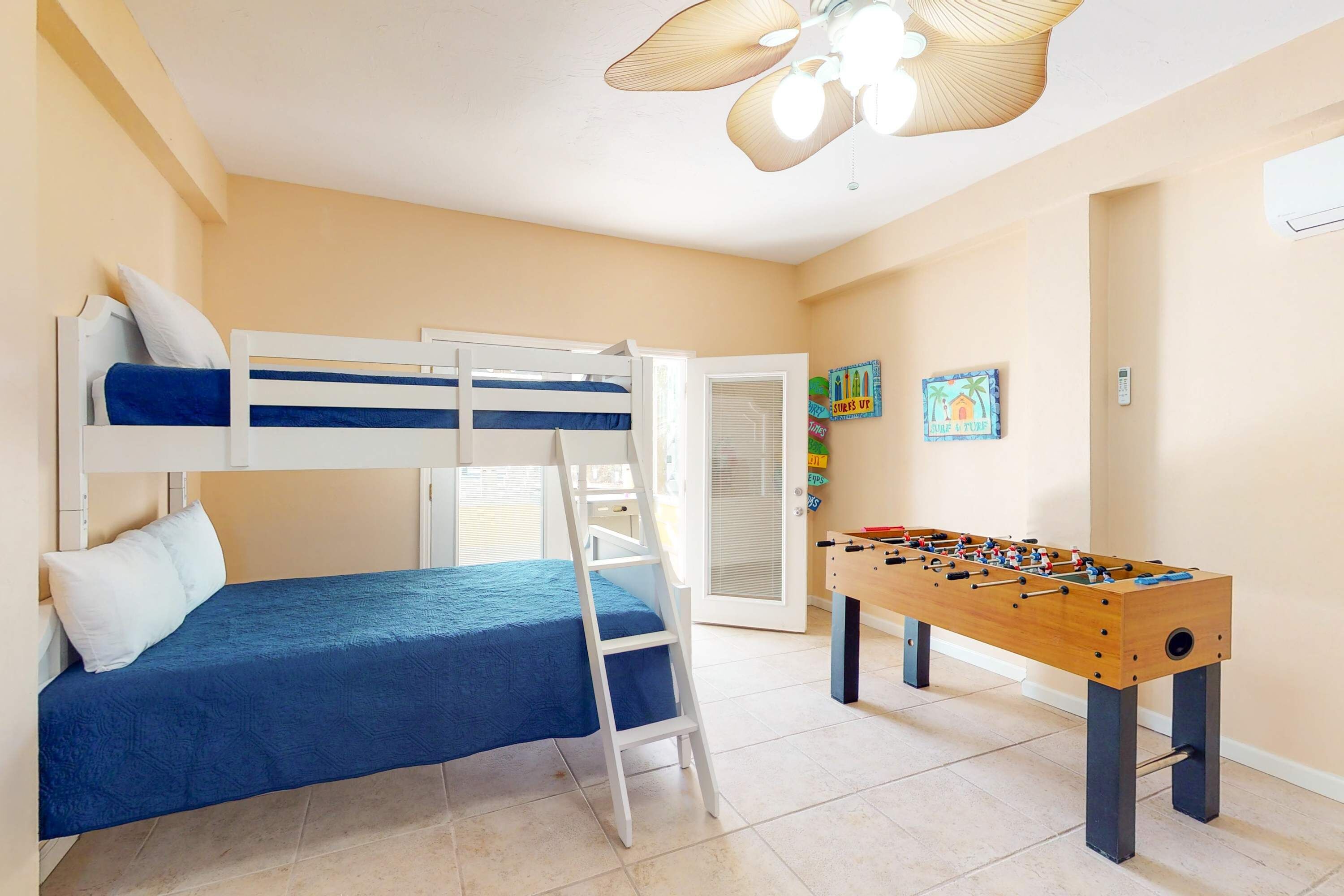 A room with bunk beds, a ladder, a foosball table, and a ceiling fan.