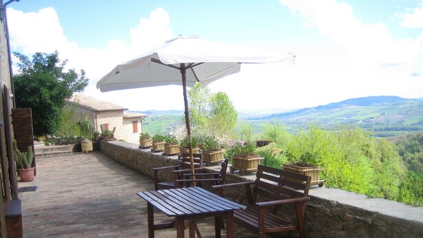Un patio al aire libre con mobiliario de madera, una sombrilla blanca y plantas en macetas.
