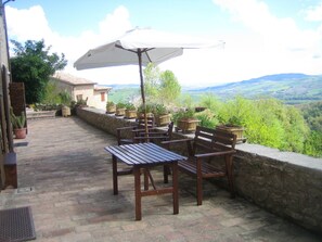 An outdoor patio with wooden furniture, a white umbrella, and potted plants. - La Valle Holiday House in Urbino. Surrounded by greenery for your exclusive use! (Urbino)