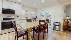 A modern kitchen with white cabinets, stainless steel appliances, and a wooden dining table with chairs. - Waterfront villa with multi level home, shared pool & easy beach access (Destin)