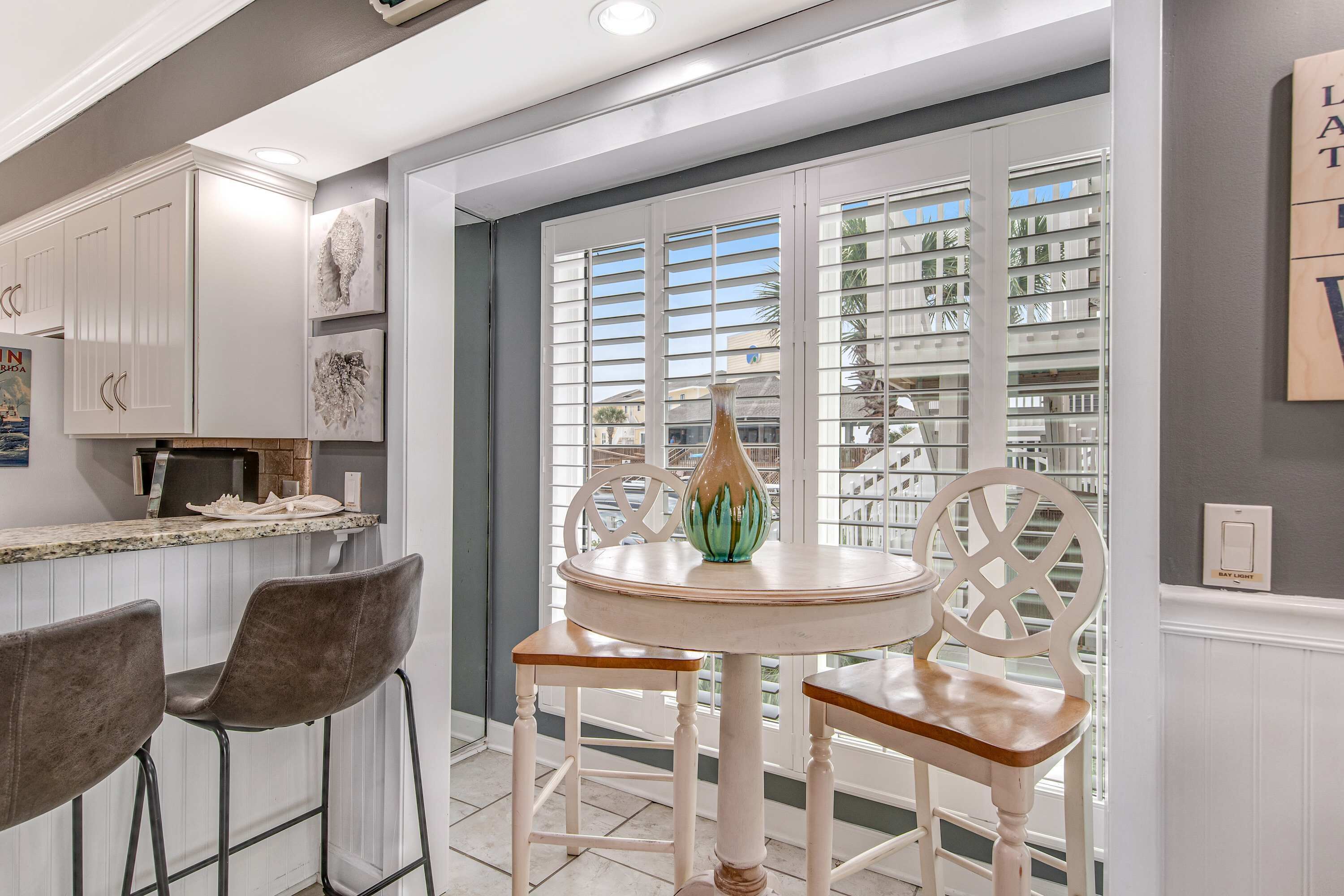 Une cuisine avec des meubles blancs, une table à manger avec des chaises et une vue par la fenêtre.