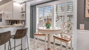 A kitchen with white cabinets, a dining table with chairs, and a view through the window.