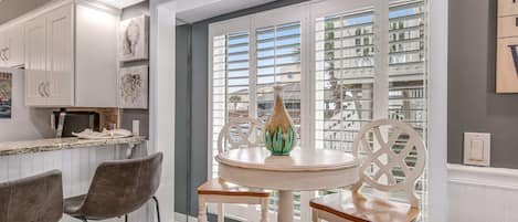 A kitchen with white cabinets, a dining table with chairs, and a view through the window.