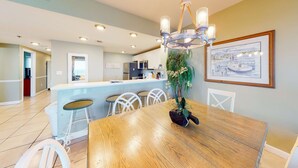 Una cocina moderna con armarios blancos, una isla central y una zona de comedor con mesa y sillas de madera.