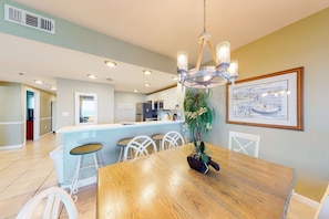 A modern kitchen with white cabinets, a central island, and a dining area with a wooden table and chairs. - Ninth Floor Oceanfront Condo with Shared Pools, Ocean View, WiFi, & Washer&Dryer (Destin)