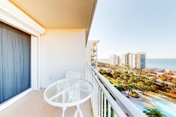 Ein Balkon mit Glastisch, Meerblick und Poolbereich.