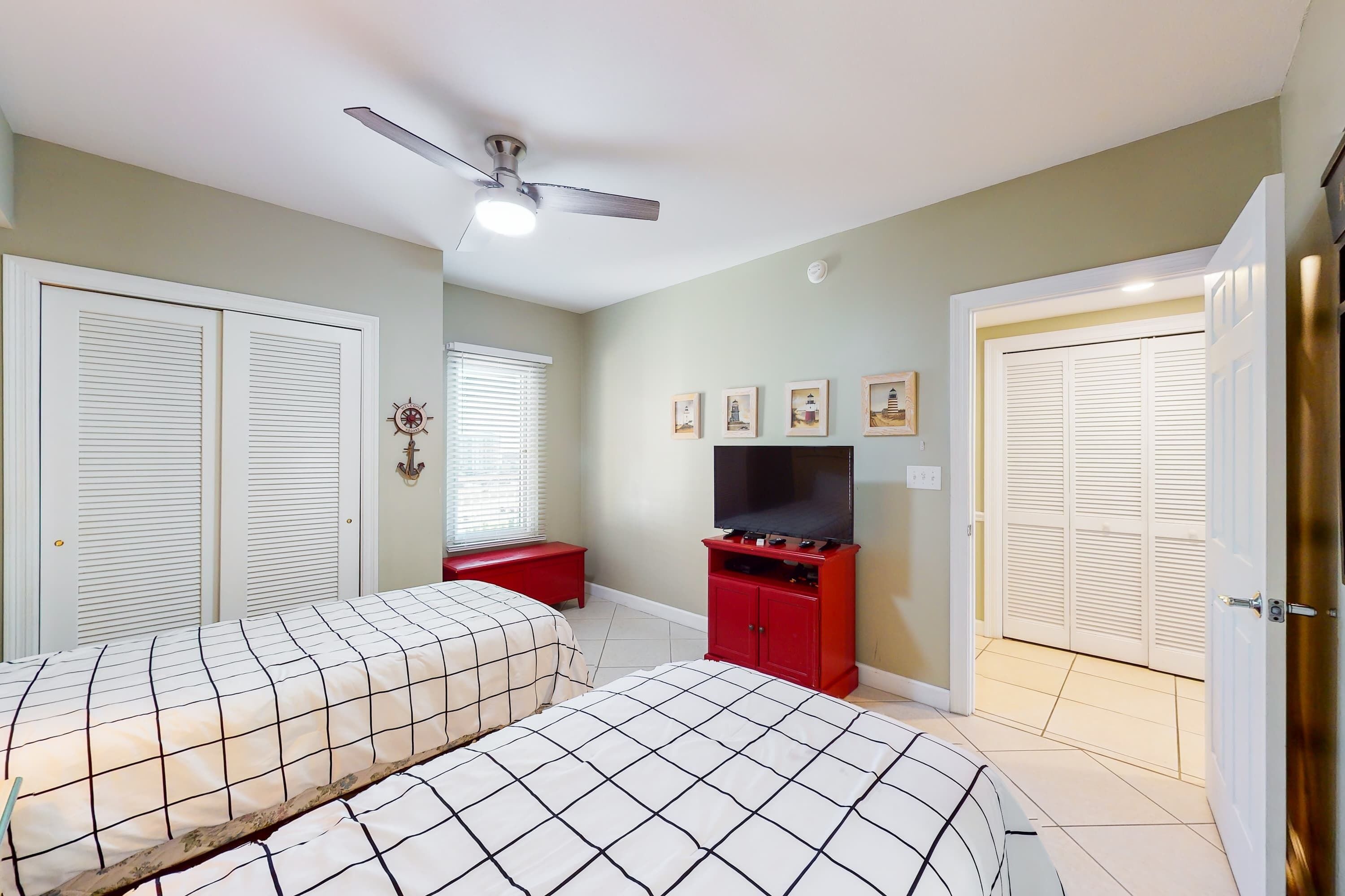 A bedroom with two beds, a TV, and a ceiling fan.