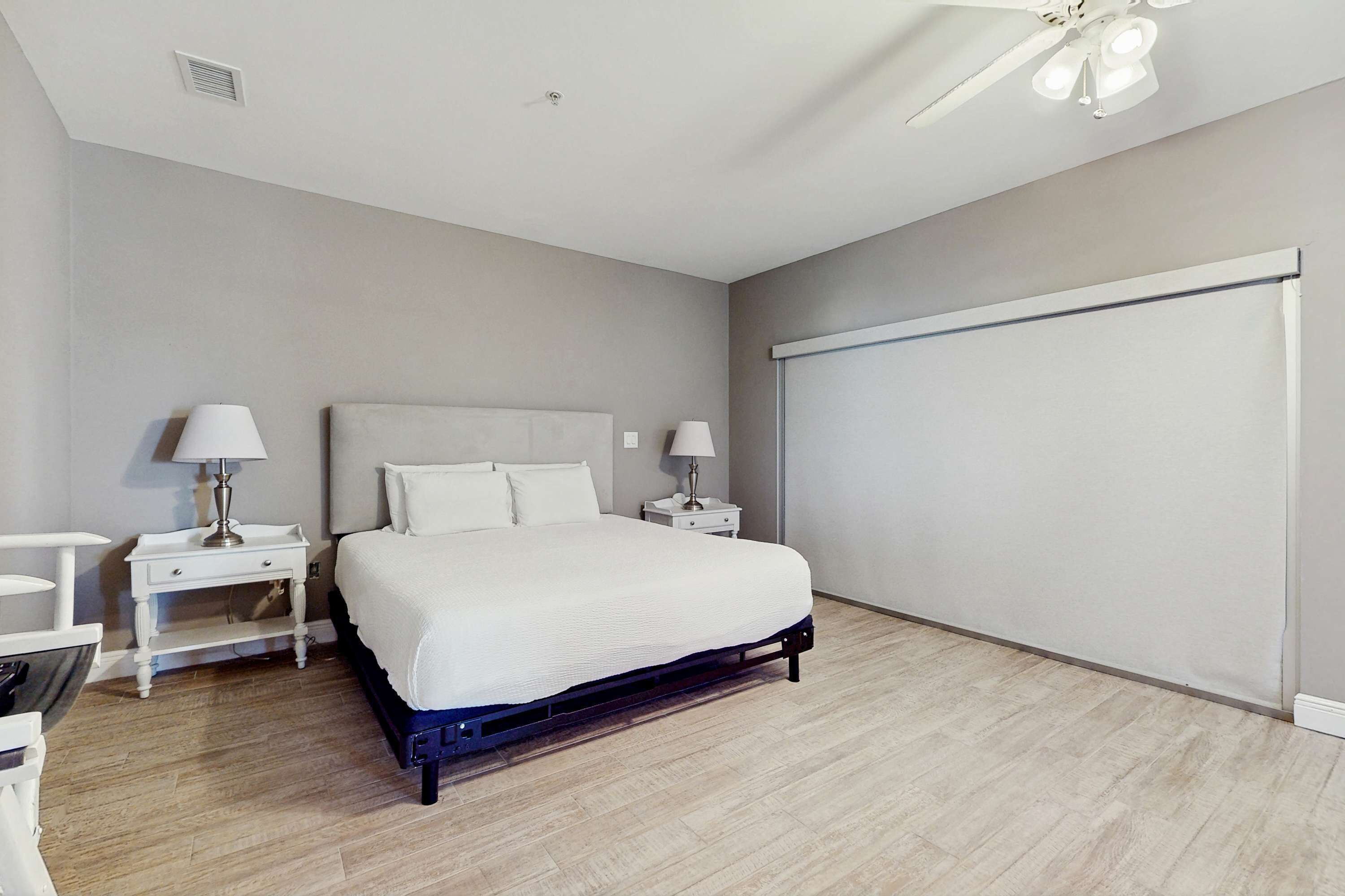 A bedroom with a bed, two bedside tables with lamps, a ceiling fan, and a large window.