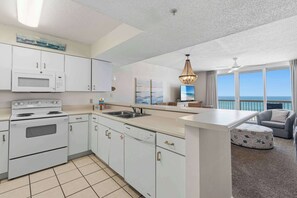 A modern kitchen with a central island, a microwave, an oven, and a dishwasher. There is a large window with a view of the ocean. - Beachfront condo with gorgeous Gulf view, balcony, pools & hot tub (Destin)