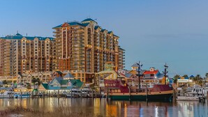A waterfront hotel with multiple buildings, a marina with boats, and a clear sky. - Emerald Grande 1025 (Destin)