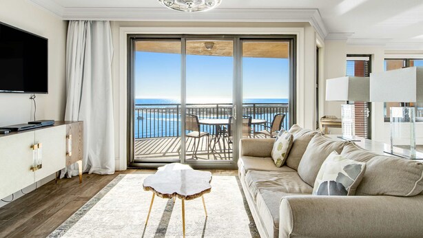 A modern living room with a large sliding glass door leading to a balcony with a view of the sea. - Emerald Grande 1025 (Destin)