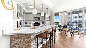 A modern kitchen with a bar area, bar stools, pendant lights, and a view of high-rise buildings. - Experience the perfect blend of luxury, comfort, and breathtaking Gulf views at Silver Shells (Destin)