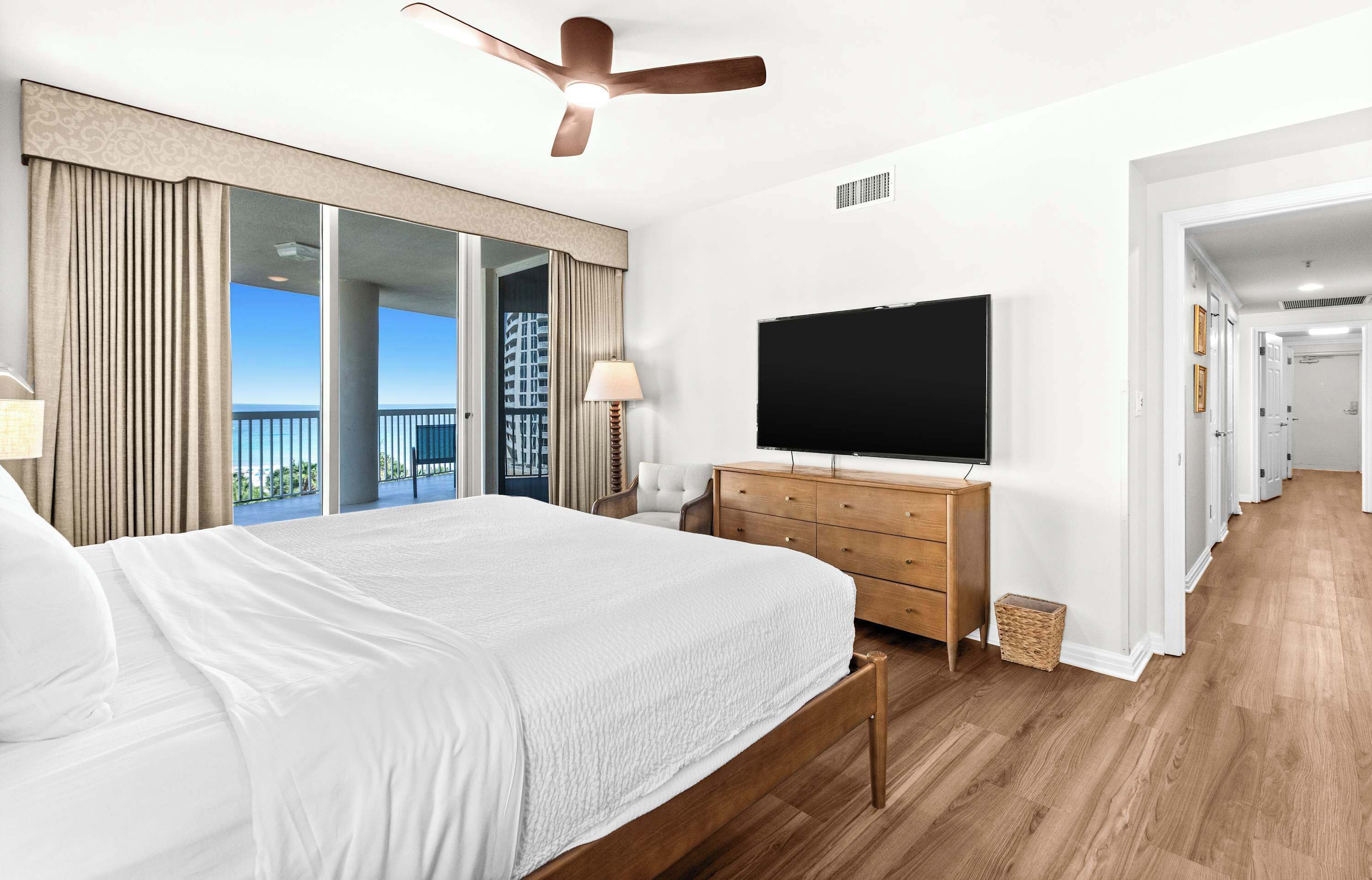 Une chambre avec un grand lit, un ventilateur de plafond, une télévision et une vue sur l’extérieur.