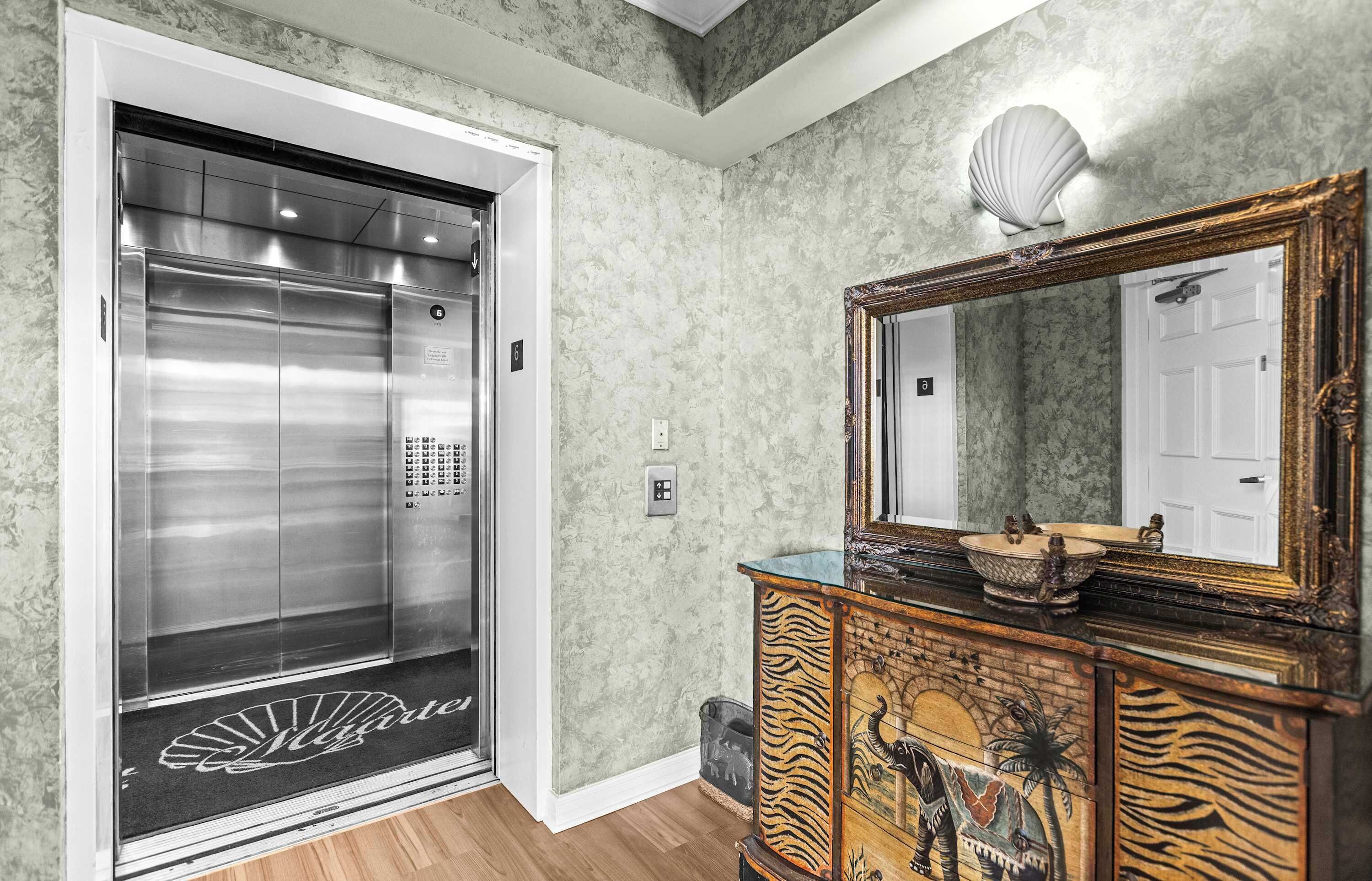 An elevator with a control panel, a mirror with a decorative frame, and a wooden cabinet with a decorative design.