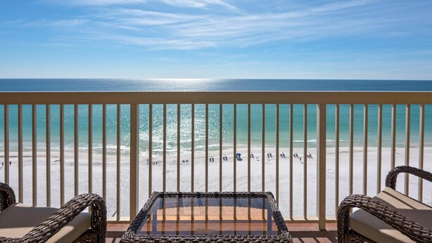 A balcony with wicker furniture overlooking a beach.
