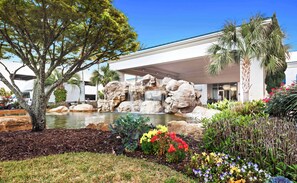 A landscaped garden with a waterfall, palm trees, and colorful flowers. - Cozy coastal condo with shared pool w lazy river and beach access (Destin)