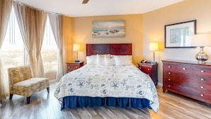 Una habitación de hotel con cama, una silla, cómoda y ventilador de techo.