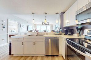 A modern kitchen with white cabinetry, stainless steel appliances, and pendant lighting. - Gorgeous beachfront condo w shared pool & beach access (Destin)