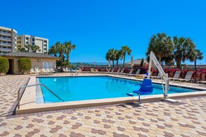 A swimming pool with a tiled deck, lounge chairs, and palm trees. - Islander 215 (Destin)