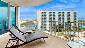 Ein Balkon mit zwei Loungestühlen und einem kleinen Tisch mit Blick auf einen Pool und ein Hochhaus.
