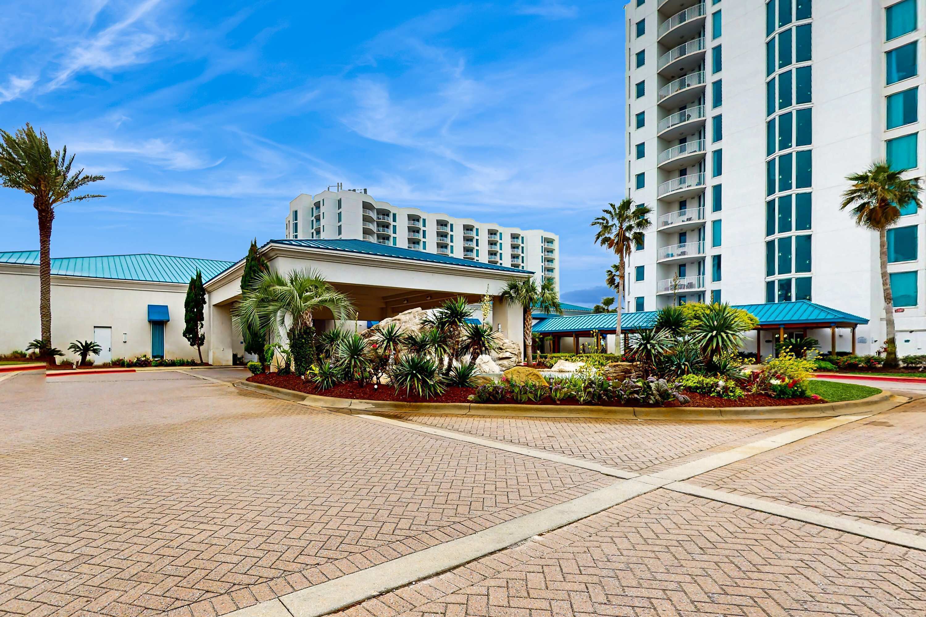 A hotel with a covered entrance, paved courtyard, and palm trees.