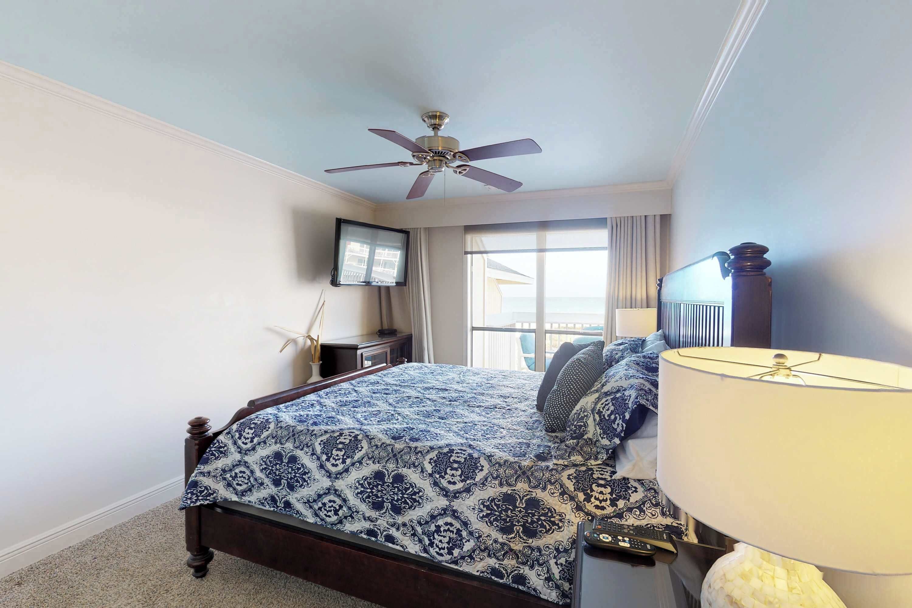A bedroom with a bed, a ceiling fan, a TV, and a window with curtains.