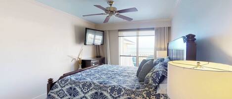 A bedroom with a bed, a ceiling fan, a TV, and a window with curtains.