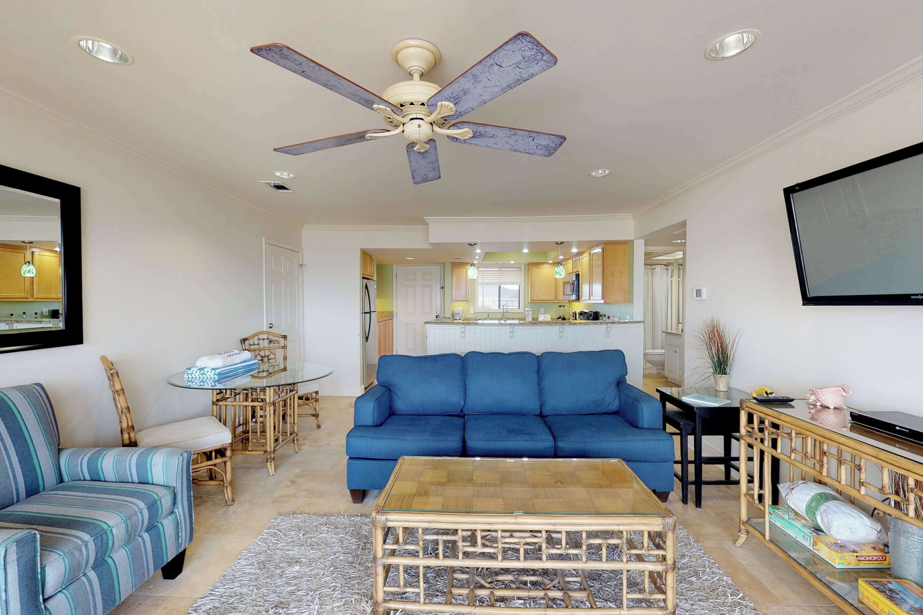 A living room with a blue sofa, a coffee table, and a ceiling fan.
