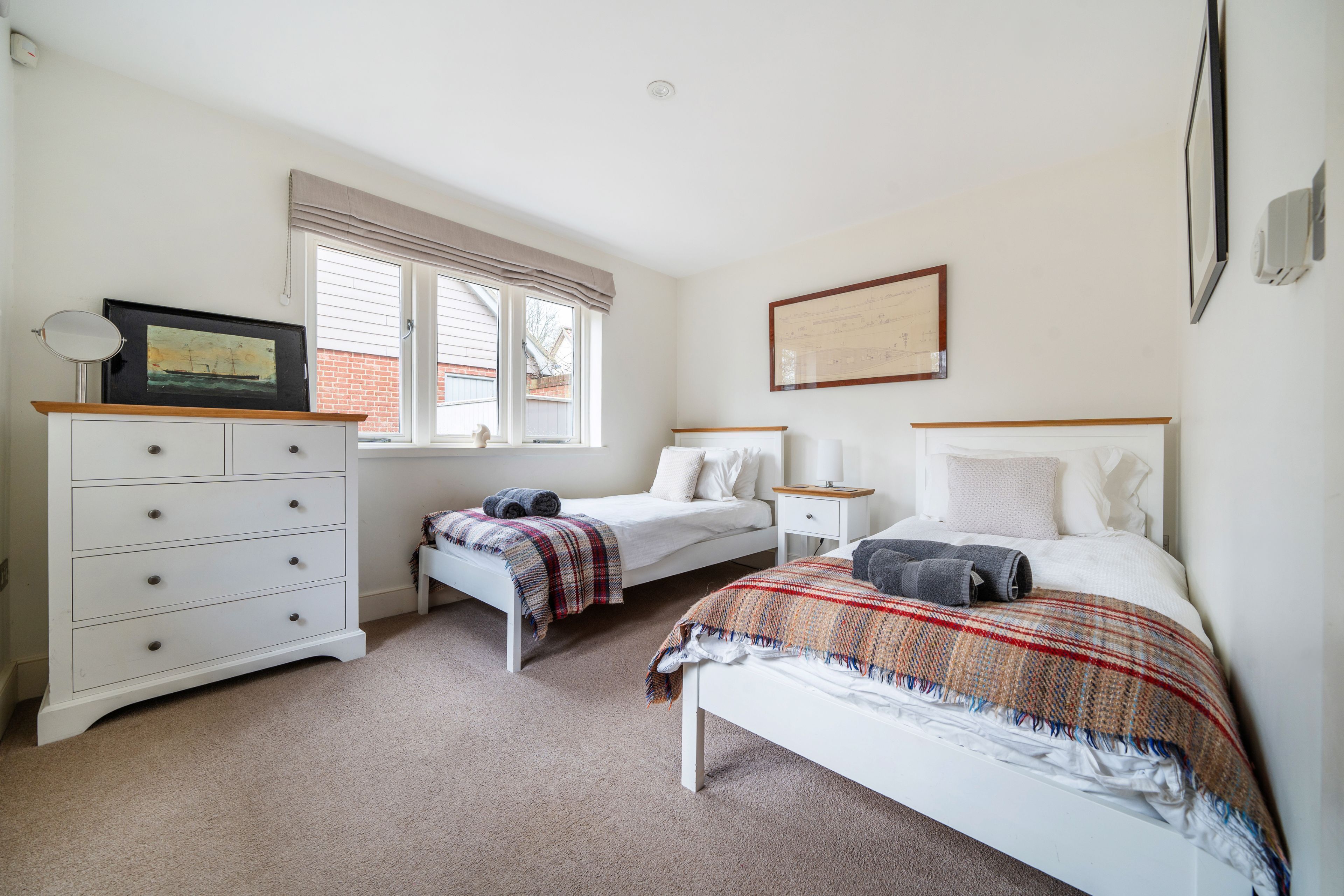 A bedroom with two beds, a dresser, a window with blinds, and a framed certificate on the wall.