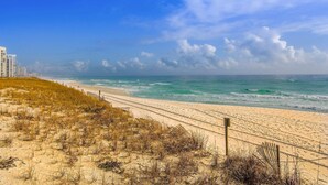 Una spiaggia con un sentiero sabbioso che conduce verso l'oceano, una recinzione in legno e un cielo azzurro terso.