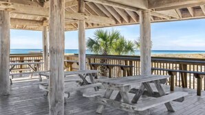 Une terrasse en bois avec des tables de pique-nique donnant sur une plage.
