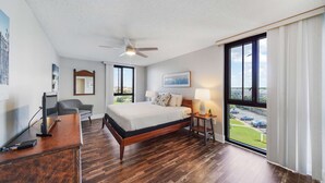 Habitación de hotel con una cama grande, un escritorio, una silla, un ventilador de techo y una ventana con vistas al exterior.