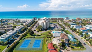 Un área residencial costera con un edificio grande, canchas de tenis y vista al océano.